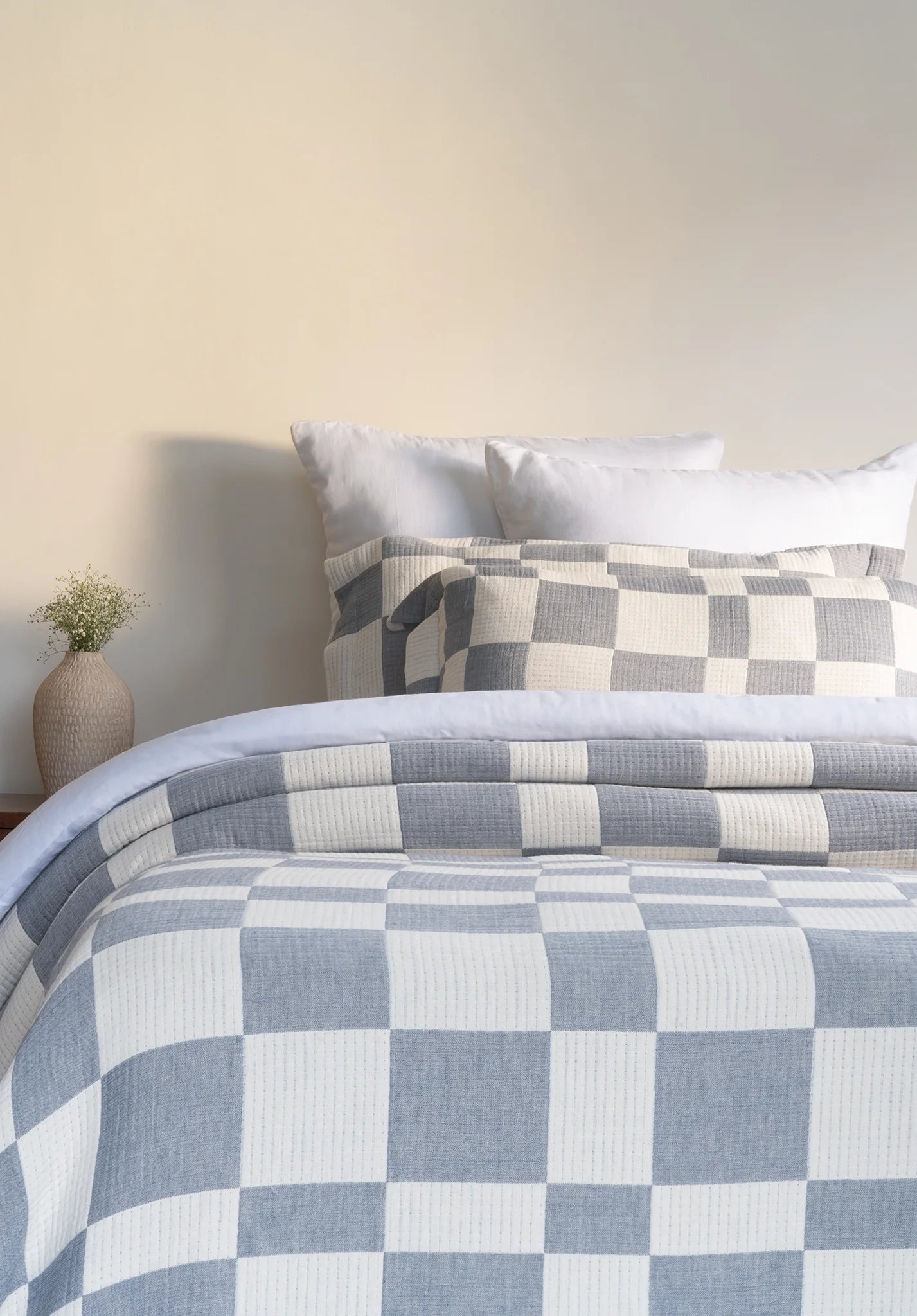 Checkered bedspread on a bed with pillows against a neutral wall.